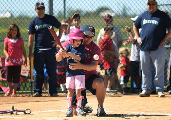 Maddy White 8, with the help of her father Derick White takes a swing at a pitch during a recent Miracle League baseball game in Lakeville. Maddy the 