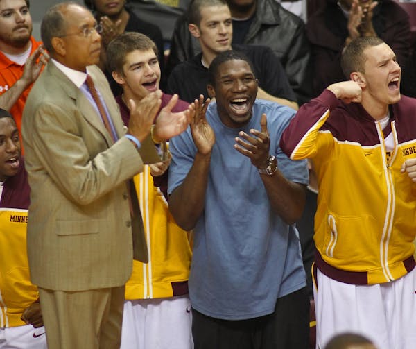 Injured Gophers player Trevor Mbakwe, center cheered on his teammates from the sideline as head coach Tubby Smith, left, looked on.