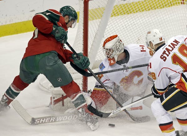 Minnesota Wild's Zach Parise, left, is thwarted in his attempt to score by Calgary Flames goalie Reto Berra in the first period of an NHL hockey game,