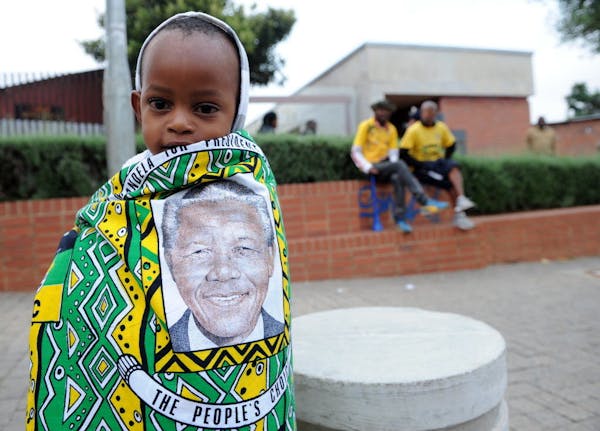 A child draped in a cloth with the image of former South African president Nelson Mandela, stands outside his former home, now museum, in Soweto, Sout