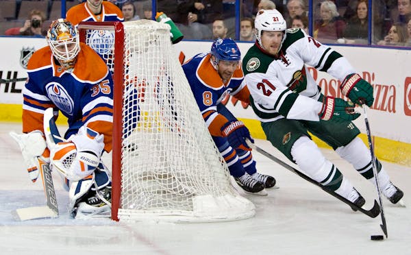 Minnesota Wild's Kyle Brodziak (21) controls the puck as Edmonton Oilers' Derek Roy (8) chases and goalie Viktor Fasth (35) looks for the shot during 