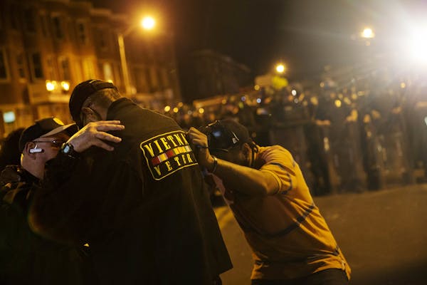 Vietnam Veteran Robert Valentine, center, prays with crowd members as police stand in riot gear ahead of a 10 p.m. curfew in the wake of Monday's riot