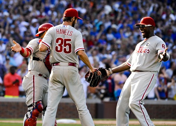Philadelphia Phillies' starting pitcher Cole Hamels (35) is hugged by Phillies' catcher Carlos Ruiz, left, and first baseman Ryan Howard after he pitc