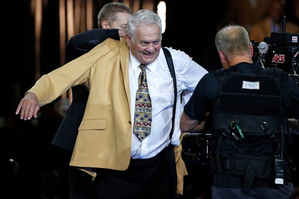 Pro Football Hall of Fame inductee Mick Tingelhoff slips on his gold jacket during the Gold Jacket Ceremony in Canton, Ohio, Thursday, Aug. 6, 2015. (