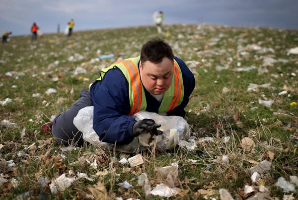 Scott Rhude, 33, sits spread-eagled in a field of garbage, reaching for a piece of trash while on a work assignment with a sheltered workshop "enclave