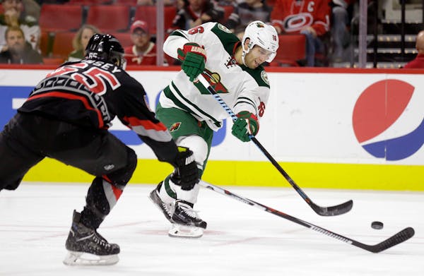 Carolina Hurricanes' Ron Hainsey, left, defends as Minnesota Wild's Jason Zucker (16) shoots during the first period of an NHL hockey game in Raleigh,