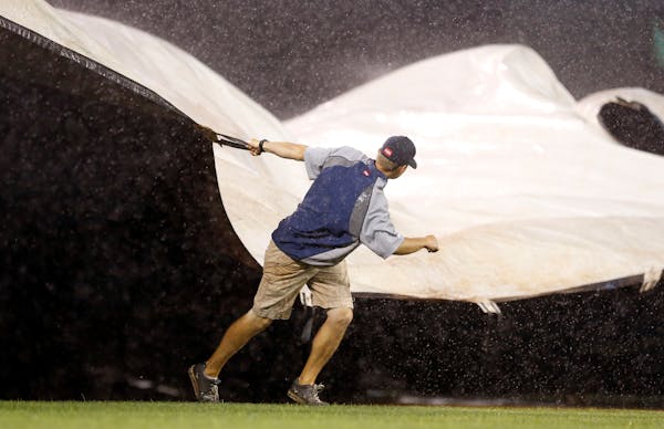 A Minnesota Twins grounds crew worker pulls the wind-blown tarp over the infield during a rain delay in the third inning of a baseball game against th