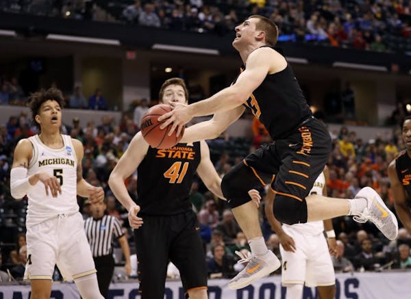 Oklahoma State's Phil Forte III, right, heads to the basket as teammate Mitchell Solomon (41) and Michigan's D.J. Wilson, left, watch during the first