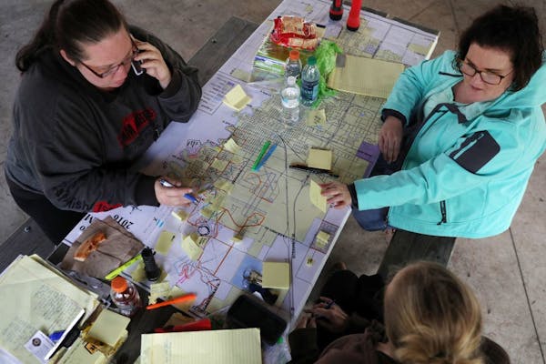 Volunteer search coordinators Christina Becker, left, Julia Wentz, right, and Bekkah Boll, bottom, sat around a map of the city of Fargo as they helpe