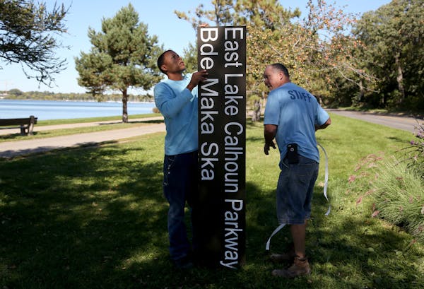 Minneapolis parks employees Dan Falk, left and Tim Coffin readied a new sign in 2015 before putting it in place near Lake Calhoun.