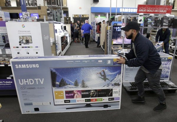 FILE - In this Nov. 23, 2017, file photo, Jesus Reyes pushes a television down an aisle as he shops at a Black Friday sale at a Best Buy store in Over