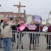 Tom Keuhn holds a cross during a Good Friday demonstration outside Planned Parenthood as pro-choice advocates held their signs on the other side of th