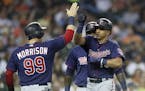 Minnesota Twins' Ehire Adrianza, right, is greeted by Logan Morrison (99) and Miguel Sano, rear, after they scored on Adrianza's grand slam during the