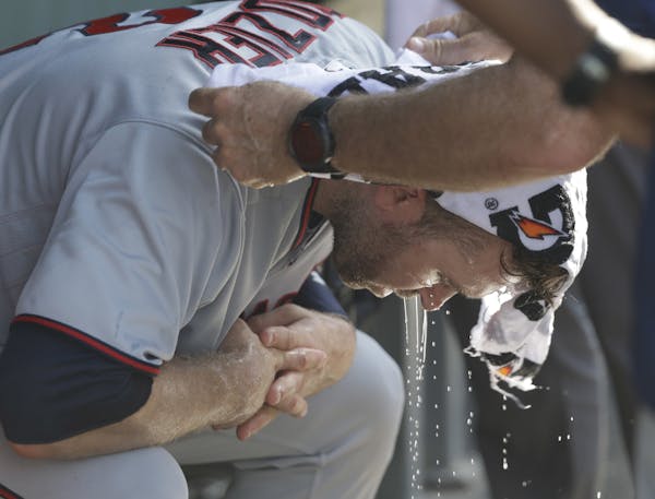 Twins second baseman Brian Dozier has a cold wet towel applied to his head during the seventh inning of Saturday's game at Wrigley Field. Temperatures