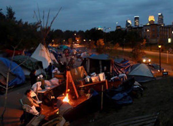Inhabitants of a large homeless camp along Hiawatha and Franklin Avenues in south Minneapolis stay warm by a fire at night.
