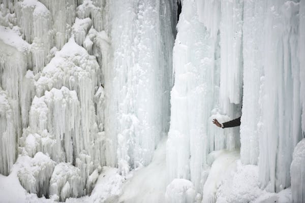 A person waves for a photo from behind frozen Minnehaha Falls Saturday, Feb. 2, 2019, in Minneapolis.