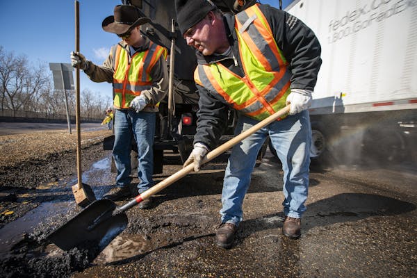 Street service workers Bradley Therres, from left, and Lance Hamby fill potholes with asphalt on Shepard Road as a truck goes by on the right side of 