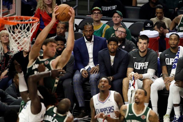 Kawhi Leonard, center, and Paul George, third from right, watch from the bench during the second half of the team's game against the Milwaukee Bucks o