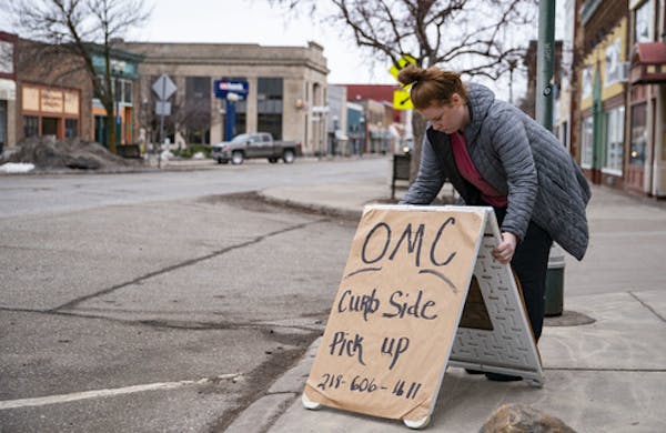 Emma Hirsch places a sign for OMC Smokehouse’s curbside pickup in front of the restaurant Wednesday morning. But Thursday owner Tom Hanson shut down