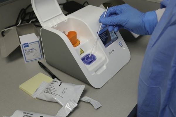 In a frame grab from video, a lab technician dips a sample into the Abbott Laboratories ID Now testing machine at the Detroit Health Center, Friday, A