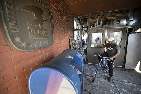 A man took photos of the burnt down U.S. post office across from the Minneapolis Police Fifth Precinct station last month. The Postal Service is explo