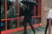 A photo from a video shows a man with an umbrella and gas mask breaking windows at the AutoZone on Lake Street in Minneapolis during riots after Georg