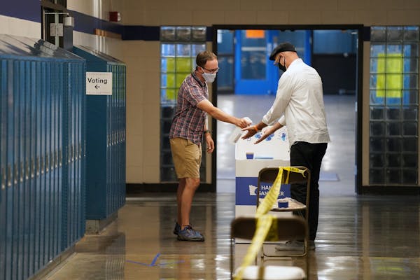 Election judge Tyler Sahnow gave a spray of hand sanitizer to John Enloe as he arrived to vote in August at Northeast Middle School in Minneapolis.