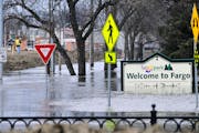 In this 2011 photo, a welcome sign for Fargo, N.D., sits in the rising floodwaters of the Red River as a flood engineer for the U.S. Army Corps of Eng
