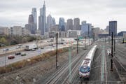 An Amtrak train departs 30th Street Station moving parallel to motor vehicle traffic on Interstate 76 in Philadelphia.