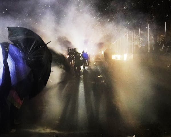 Protesters walk amid tear gas launched by nearby law enforcement officers outside the Brooklyn Center Police Department during the third night of unre