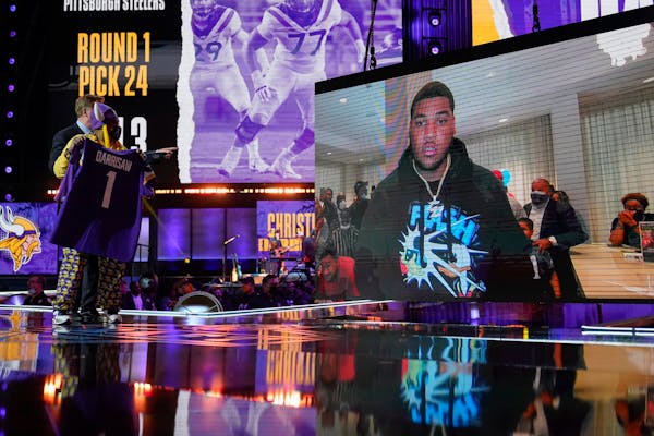 A Minnesota Vikings fan, left, holds a team jersey as an image of Christian Darrisaw is shown on stage at the draft in Cleveland.