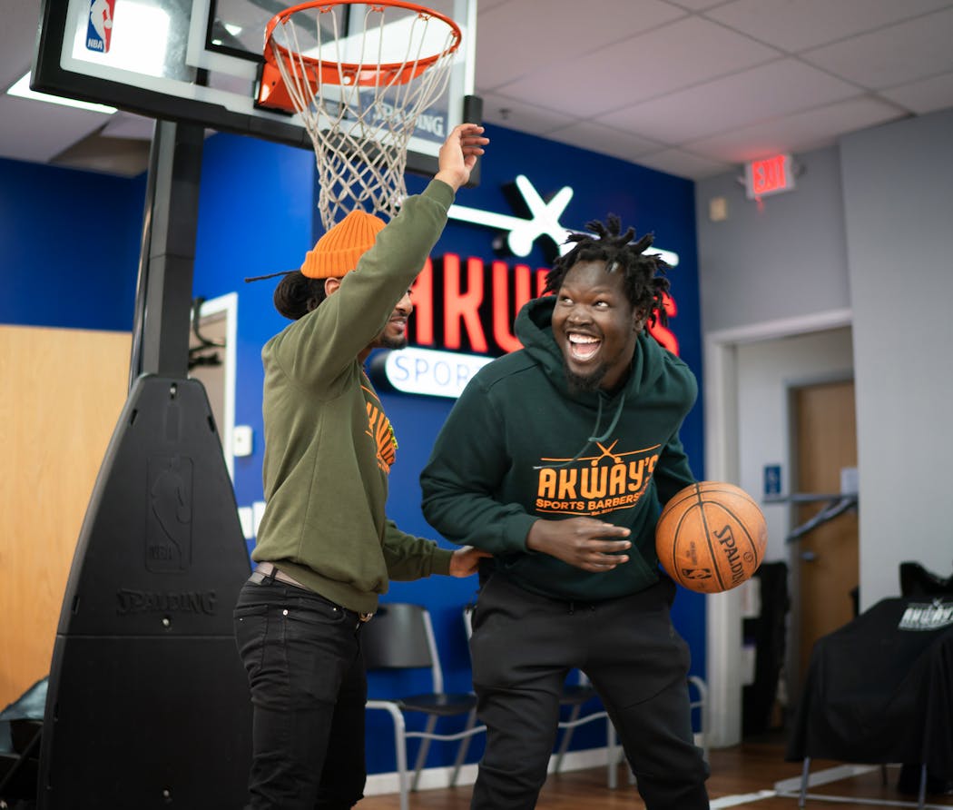Akeem Akway, right, shoots hoops during some down time at their barbershop with cousin and business partner, Nathan Sheferaw.