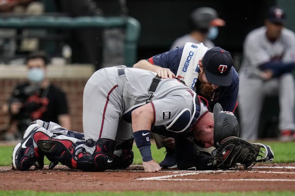 Twins assistant athletic trainer Matt Biancuzzo talks to catcher Mitch Garver after he took a foul ball from Orioles designated hitter Trey Mancini du
