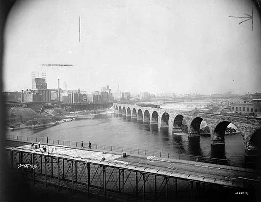 A view of St. Anthony Falls flour milling district, and the repair of the 10th Avenue Bridge in Minneapolis around 1900.