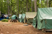 A typical campsite at a Boy Scout Camp includes tents, a table, dirt, and dirty clothes drying on a rope.