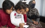 Bayan, left, Safa, center, and Iman play with a cellphone as they sit next to their mother Kariman, 32 at their apartment in the northern city of Thes