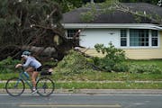 A woman rode her bike past a home with uprooted trees and storm damage after overnight storms with high winds rolled through the area in Richfield.