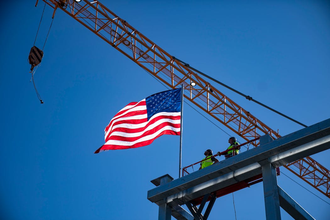 Matt Hilton, left, and Darren Silvernagel unfurled the American flag after securing the final steel beam on the roof of the new RBG Gateway tower in Minneapolis.