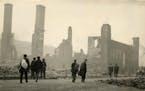 People walking in front of a destroyed school building after the fires of 1918.  