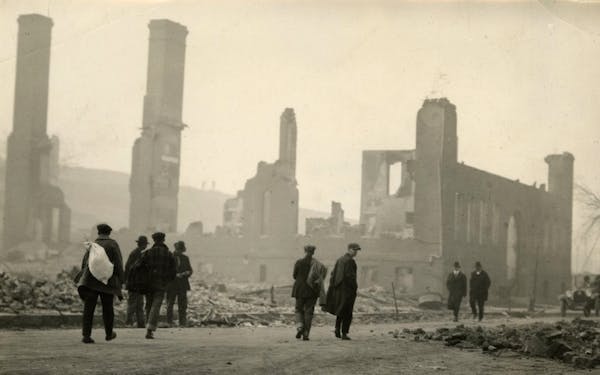 People walking in front of a destroyed school building after the fires of 1918.  
