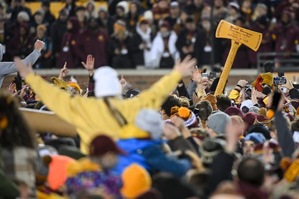 Fans celebrate with Paul Bunyan’s Axe after storming the field after an NCAA football game between the Gophers and the Wisconsin Badgers.