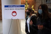 People pass a sign that reads “Face Mask Required” in a mall as COVID-19 cases surge in the city, on Tuesday, Dec. 21, 2021 in Washington, D.C. Di