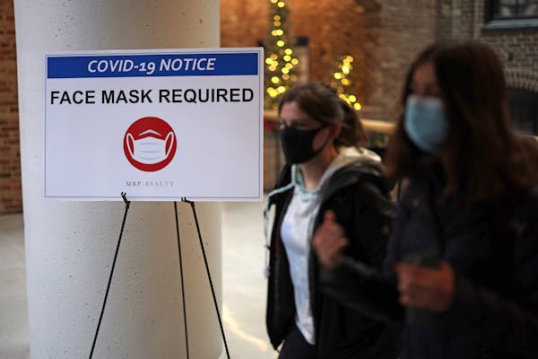 People pass a sign that reads “Face Mask Required” in a mall as COVID-19 cases surge in the city, on Tuesday, Dec. 21, 2021 in Washington, D.C. Di