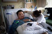 Troy Chang, 9, watched cartoons Friday while recovering from severe COVID-19 as his mom, Linda Vang, checked his breathing and feeding tubes at HCMC i