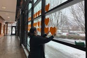 Jasmine Robles hangs two more hearts on the COVID-19 memorial at Edina City Hall. There are 113 golden hearts in the window. One for every resident lo