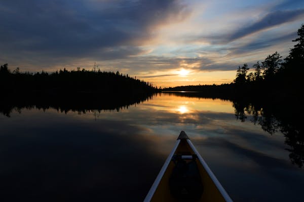 The sun set in front of the bow of a Wenonah Minnesota II canoe in the Boundary Waters Canoe Area Wilderness on Eddy Lake in Fall Lake Township in 202