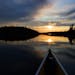 The sun set in front of the bow of a Wenonah Minnesota II canoe in the Boundary Waters Canoe Area Wilderness on Eddy Lake in Fall Lake Township in 202