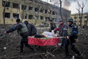 Ukrainian emergency employees and volunteers carry an injured pregnant woman from a maternity hospital damaged by shelling in Mariupol, Ukraine, on Ma