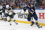 Scott Perunovich of the Blues moved the puck with Wild center Ryan Hartman in pursuit on Sunday in St. Louis.