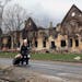 A woman pulls her bags past houses damaged during fighting in eastern Mariupol, Ukraine, Friday, April 8, 2022. Ukraine says it is investigating a cla
